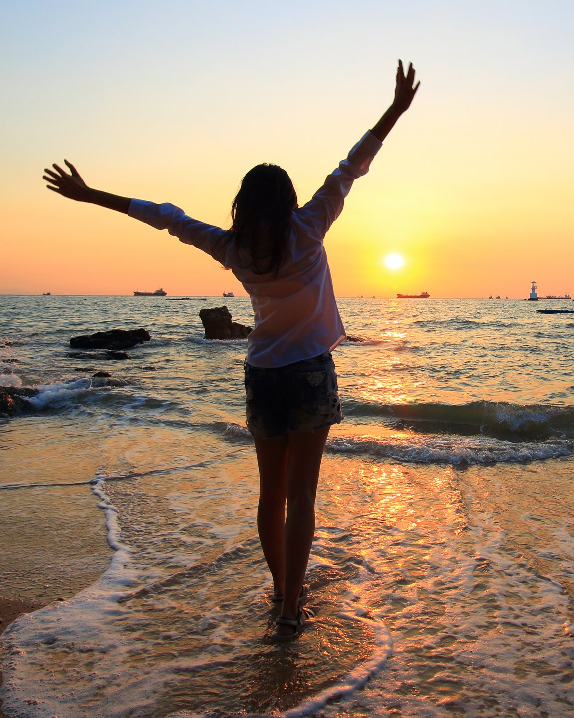 A woman on a beach at sunset, arms raised